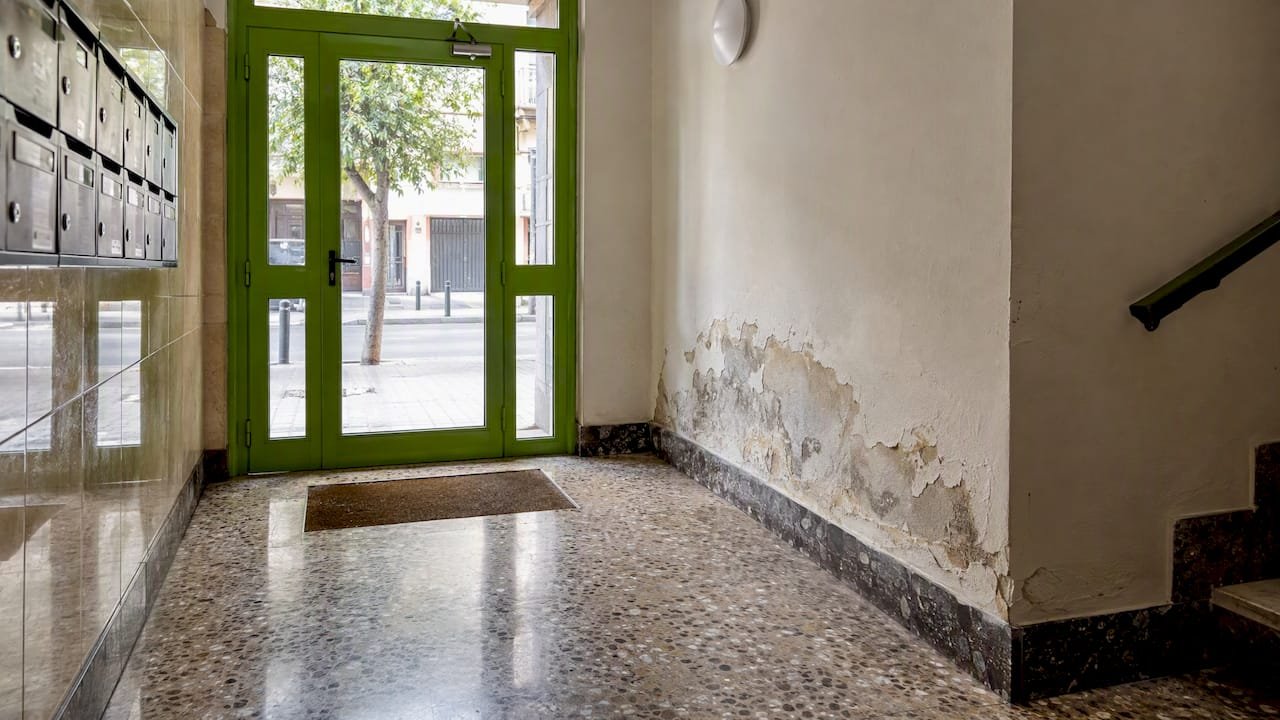 Portal de la comunidad con humedad en el muro inferior